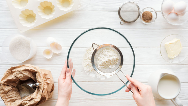 cropped view of woman sieving flour in bowl on table with ingredients - Foto, Bild