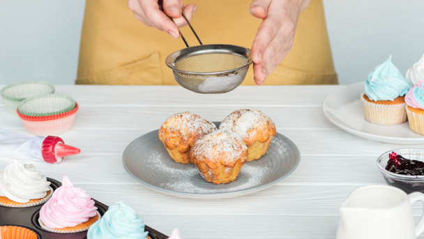 Vista recortada de la mujer decorando cupcakes con azúcar en polvo aislado en gris
 - Foto, Imagen
