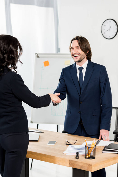handsome recruiter shaking hands with brunette woman in office  - Fotografie, Obrázek