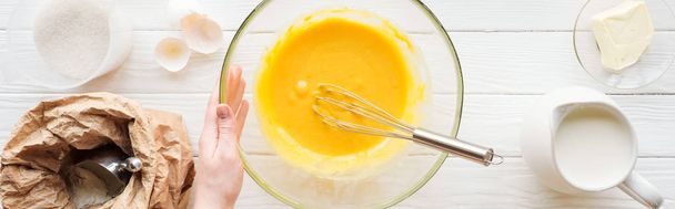 panoramic shot of woman holding bowl with balloon whisk and liquid dough on table - Photo, image