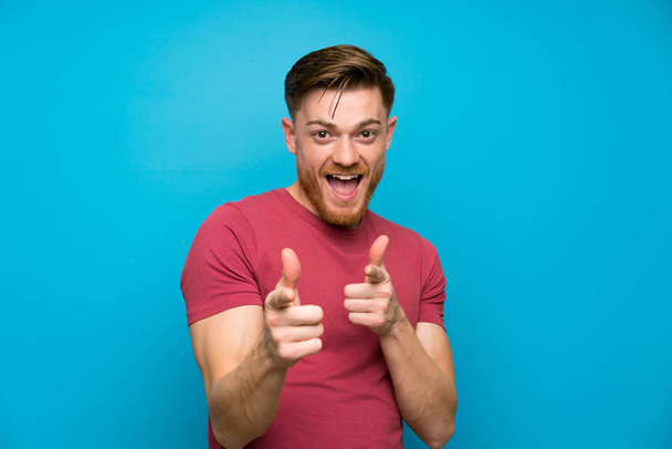 Redhead man op geïsoleerde blauwe muur punten vinger op je - Foto, afbeelding