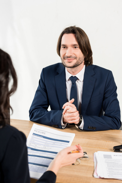 selective focus of smiling man with clenched hands looking at recruiter with resume  - Fotografie, Obrázek