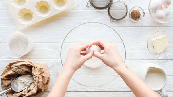 visão parcial da mulher rachando ovo na tigela enquanto cozinha na mesa
 - Foto, Imagem