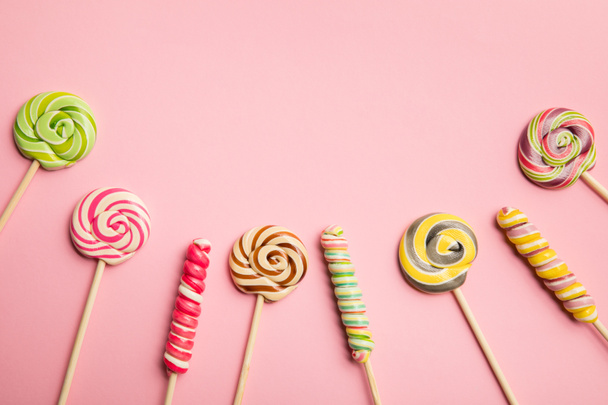 top view of multicolored swirl lollipops on wooden sticks on pink background - Fotoğraf, Görsel