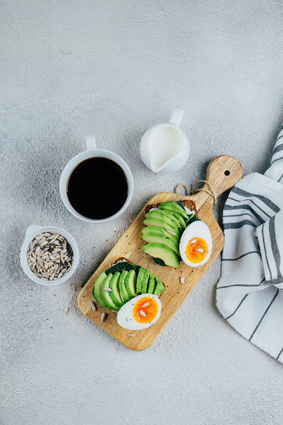 Delicious avocado toast on dark rye grain bread on wooden cutting board and cup of black coffee on concrete background. Healthy Breakfast Concept. View From above, top view, copy space. - Photo, image