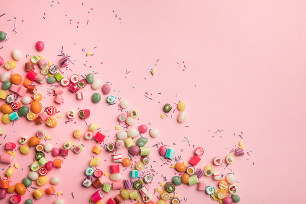 vista superior de coloridos caramelos y salpicaduras esparcidas sobre fondo rosa con espacio de copia
 - Foto, imagen
