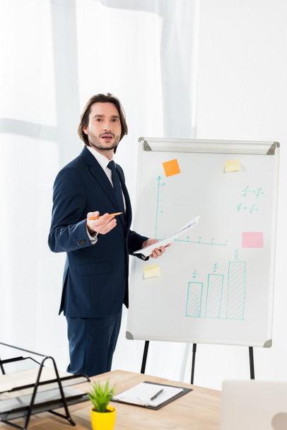 selective focus of handsome man in formal wear holding paper and standing near white board  - Photo, Image