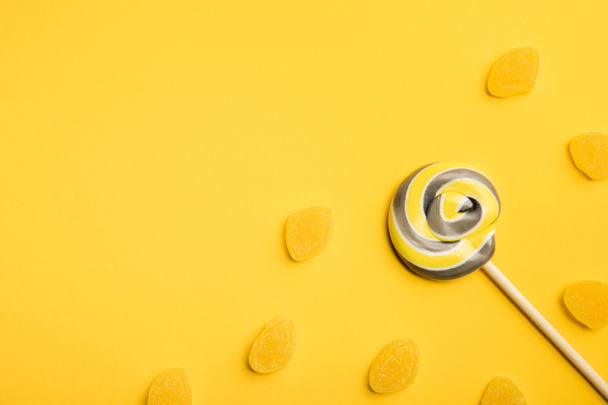 top view of delicious multicolored swirl lollipop on wooden stick and jellies on yellow background - Foto, Bild