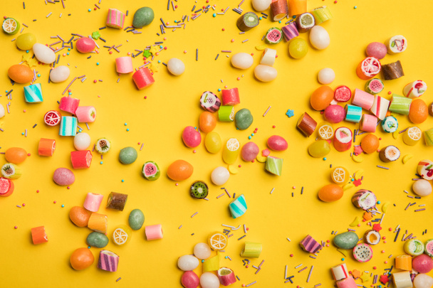 top view of multicolored candies and sprinkles scattered on yellow background  - Foto, immagini