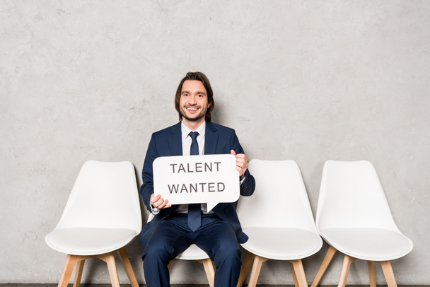happy recruiter sitting on chair and holding speech bubble with talent wanted lettering  - 写真・画像