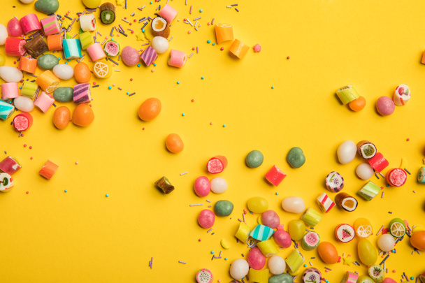 top view of multicolored tasty sweets scattered on yellow background with copy space - Foto, immagini