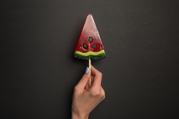 cropped view of woman holding watermelon tasty lollipop on black background - Photo, image