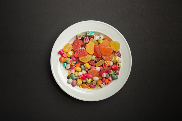 vue du dessus de délicieux bonbons au caramel multicolores et gelées d'agrumes en plaque blanche sur fond noir
  - Photo, image