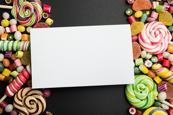 top view of delicious multicolored sweets and blank white card on black background - Photo, Image