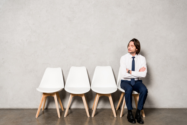 όμορφος άντρας καθισμένος στην καρέκλα με σταυρωτά χέρια, περιμένοντας συνέντευξη για δουλειά  - Φωτογραφία, εικόνα