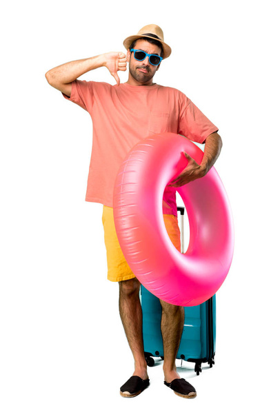 Повне тіло людини з капелюхом і сонцезахисними окулярами на літніх канікулах показує великий палець вниз обома руками. Негативний вираз на ізольованому фоні
 - Фото, зображення