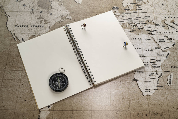Δύο μικρές μινιατούρες σε λευκό σημειωματάριο με πυξίδα στον παγκόσμιο χάρτη - Φωτογραφία, εικόνα