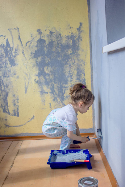 Little kid girl paints wall by paint roller. - Photo, Image