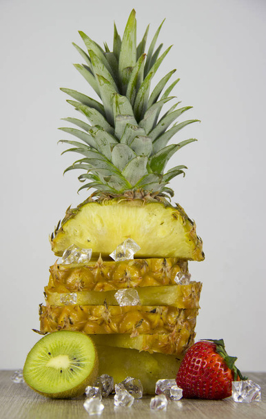 Szeletelt ananász az asztalon, világos háttér. Válogatott szamóca, Kiwi és ananász. - Fotó, kép