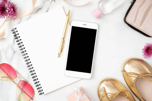 Flat lay home office desk. Female workspace with mobile phone, paper notepad, golden shoes and feminine accessories on marble background. Fashion blog banner. Beauty blogger desk concept. Top view - Foto, afbeelding