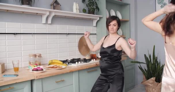 Dos mujeres embarazadas en pijama bailando y comiendo magdalenas en la cocina
. - Imágenes, Vídeo