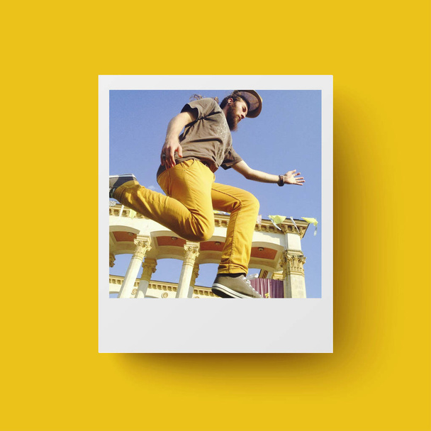 Sarı arka planda Anlık Fotoğraf kartı. Kartpostal, seyahat konsepti. Mutlu genç sakallı adam sokakta atlama - Fotoğraf, Görsel