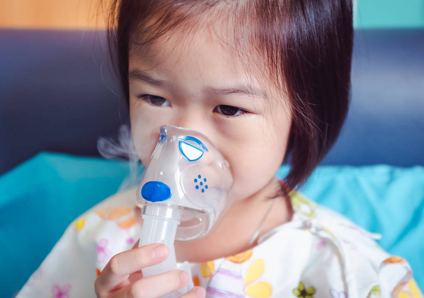 Üzgün asyalı çocuk astım tedavisi için bir maske buharı inhaler tutar. Buharlı nebülizörden nefes alıyor. Hasta kız hastaneye başvurdu. - Fotoğraf, Görsel