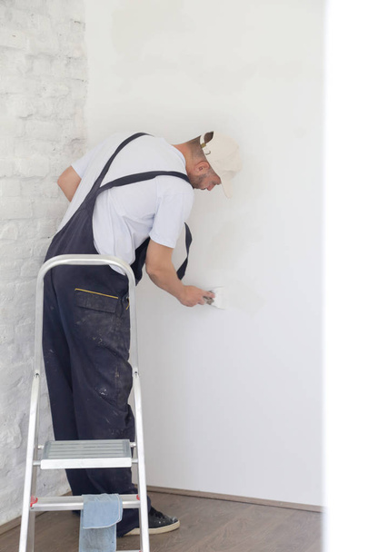 Hombre enyesando la pared con masilla-cuchillo, imagen de cerca. Fijación de la superficie de la pared y preparación para la pintura
. - Foto, Imagen