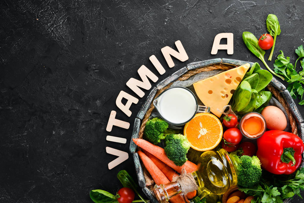 Alimentos que contienen vitamina A natural: brócoli, zanahorias, leche, queso, espinacas, albaricoques, perejil, tomates. Sobre un fondo de cocina de piedra negra. Vista superior
. - Foto, imagen