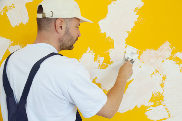 Hombre enyesando la pared con masilla-cuchillo, imagen de cerca. Fijación de la superficie de la pared y preparación para la pintura
. - Foto, Imagen