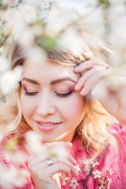 Spring portrait of a young blonde near a flowering tree. Happy young woman. - Photo, Image