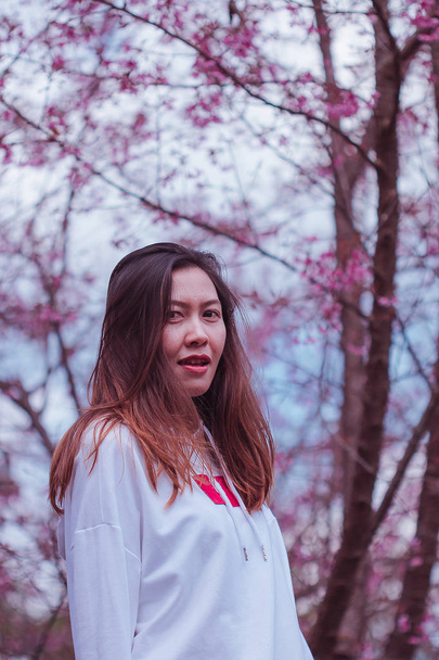 Женщина носила белую рубашку под розовым деревом зимой.
. - Фото, изображение