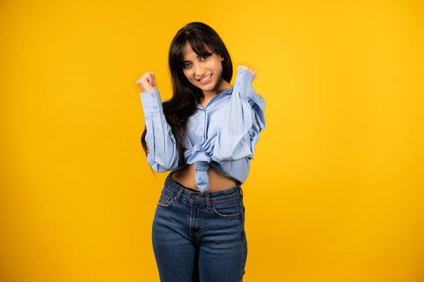 Young beautiful girl in a blue shirt posing for a photo on a yellow background. - Foto, Imagem