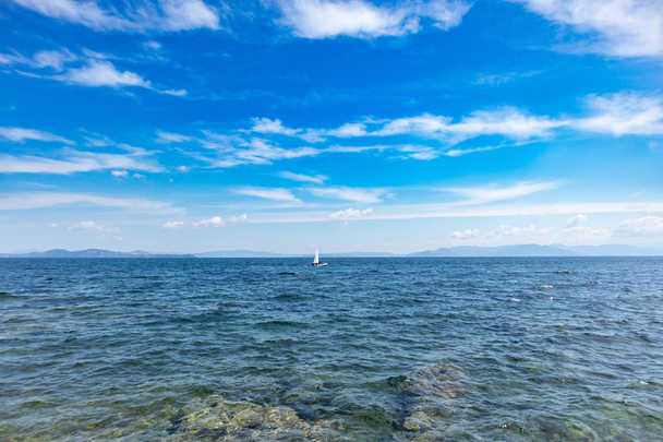 Kis optimista csónak, fehér vitorlát, kék ég és a tenger háttér - Fotó, kép