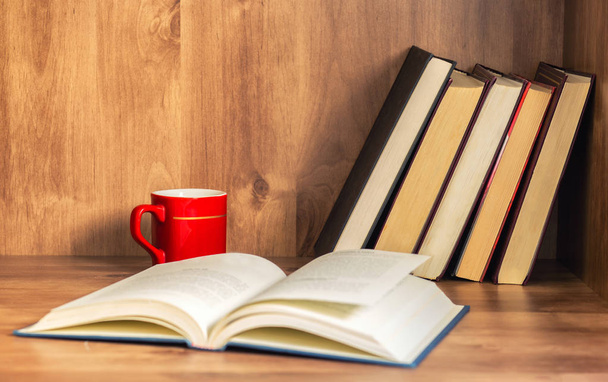 Montón de libros cerrados y libro abierto con taza de café sobre fondo de madera
. - Foto, Imagen
