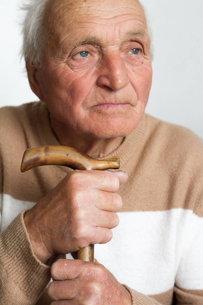 Porträt eines alten, traurigen Mannes, der seinen Kopf auf den Griff eines Holzstockes legt. - Foto, Bild