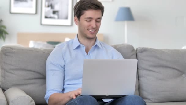 Online chat βίντεο για το laptop από τον όμορφο νεαρό άνδρα που κάθεται στο δημιουργικό χώρο εργασίας - Πλάνα, βίντεο