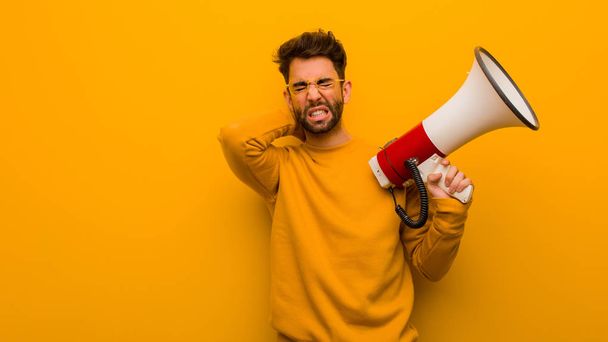 Young man holding a megaphone suffering neck pain - Photo, Image