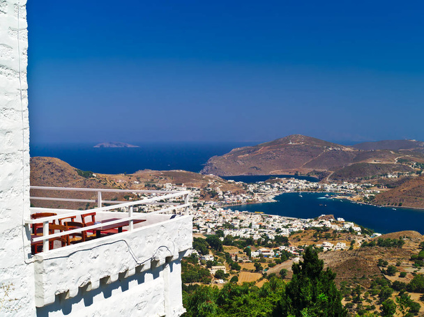 Distant view of Skala village on Patmos island in Greece. Traditional house balcony on foreground. Summer deep blue sky. - Photo, Image