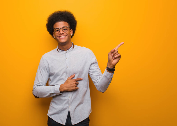 junger afrikanisch-amerikanischer Mann über eine orangefarbene Wand, die mit dem Finger zur Seite zeigt - Foto, Bild