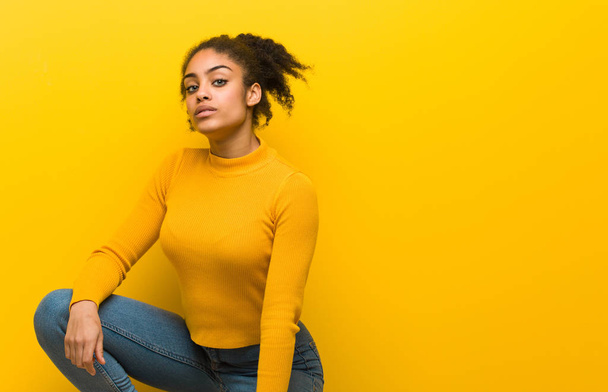 オレンジ色の壁の上に座っている若い黒人女性 - 写真・画像