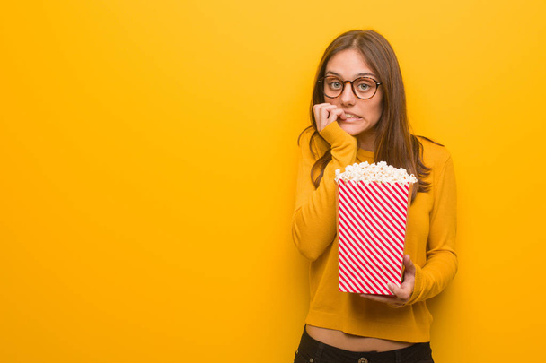 Young pretty caucasian woman biting nails, nervous and very anxious. She is eating popcorns. - Foto, Imagen