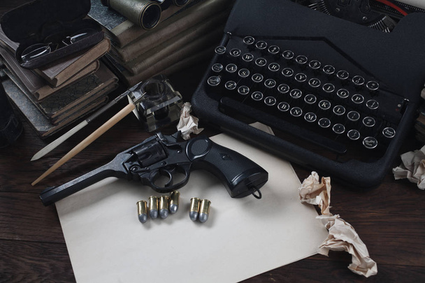 Krimischreiben - alte Retro-Oldtimer-Schreibmaschine und Revolverpistole mit Munition, Büchern, Blankopapier, altem Tintenstift - Foto, Bild