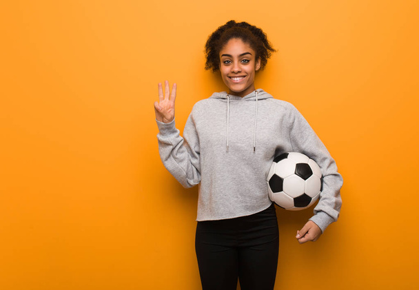 Молодая черная женщина показывает номер три. Холдинг футбольный мяч
. - Фото, изображение