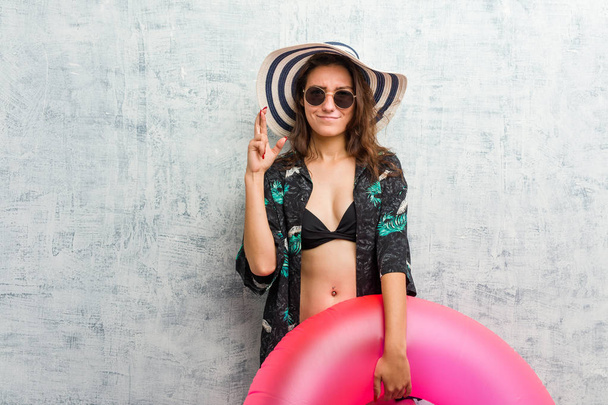 Young european woman holding a inflatable donut crossing fingers for having luck - Foto, Imagen