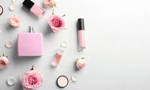 Flat lay composition with bottles of perfume, cosmetics and roses on grey background. Space for text - Photo, image