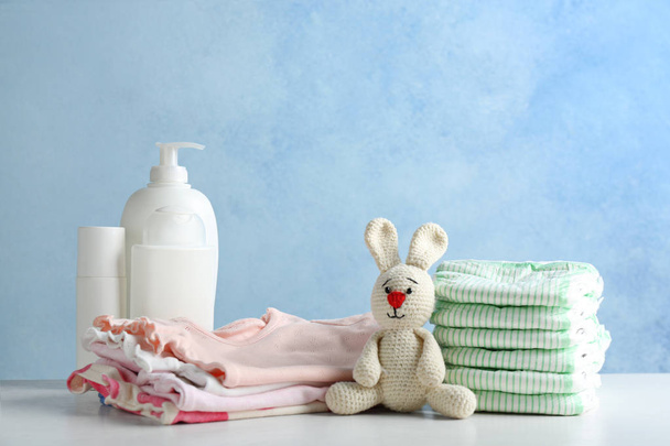 Stack of diapers and baby accessories on table against color background. Space for text - Zdjęcie, obraz