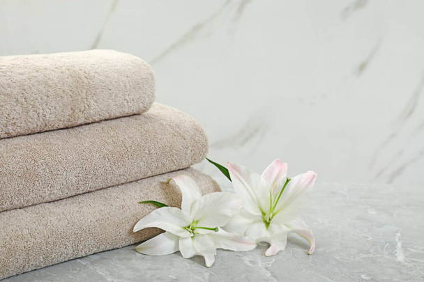 Stack of fresh towels with flowers on grey table against light background. Space for text - Фото, зображення