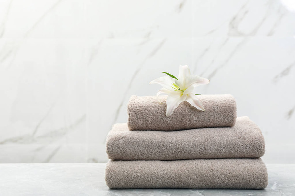Stack of fresh towels with flower on grey table against light background. Space for text - Фото, изображение