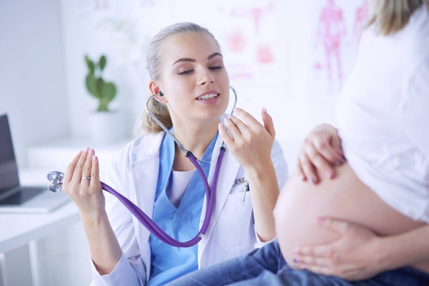 Young woman doctor with stethoscope speaking with pregnant woman at hospital. - Foto, Imagen